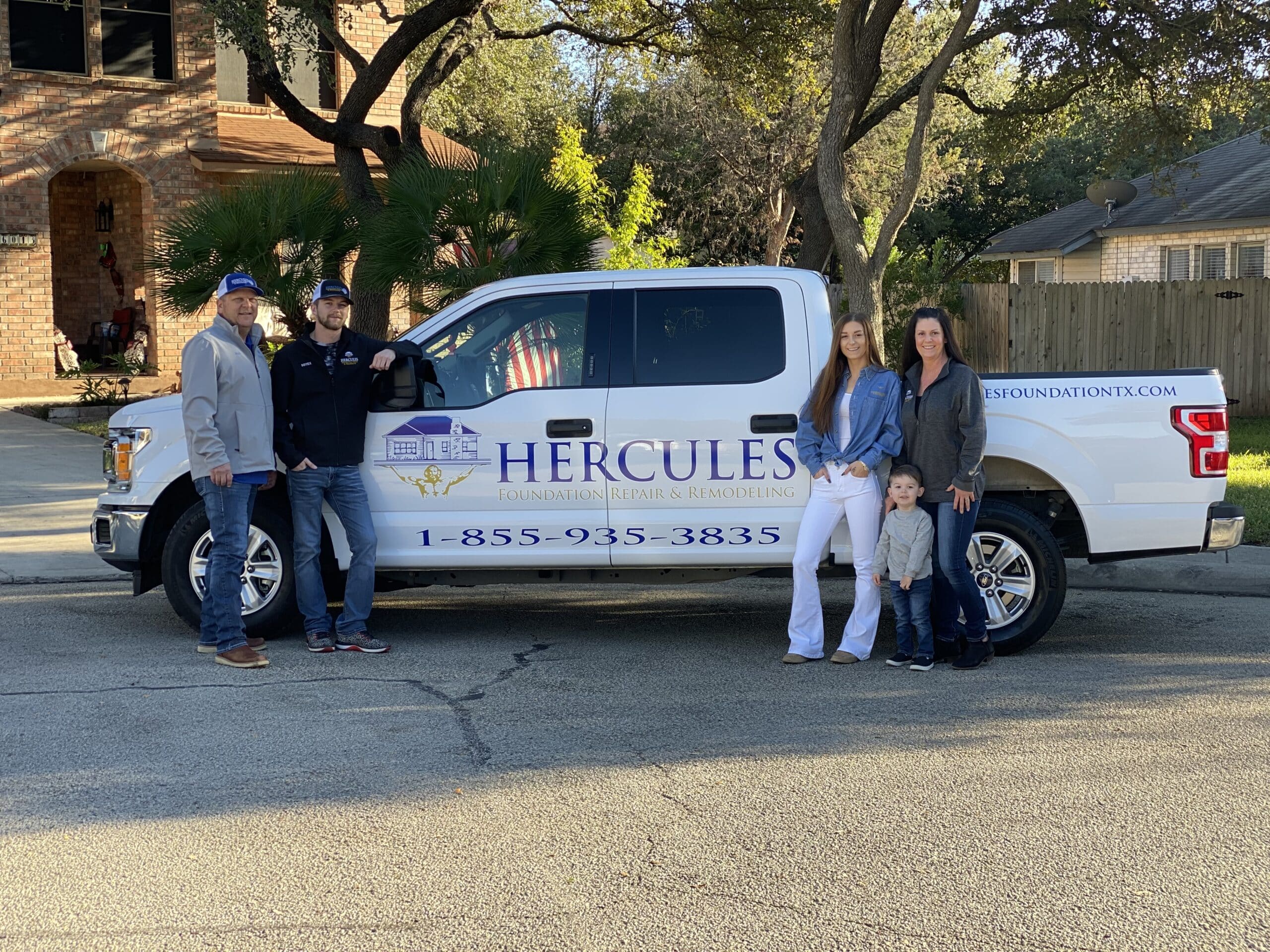 Hercules foundation repair family standing around company branded truck and smiling at the camera
